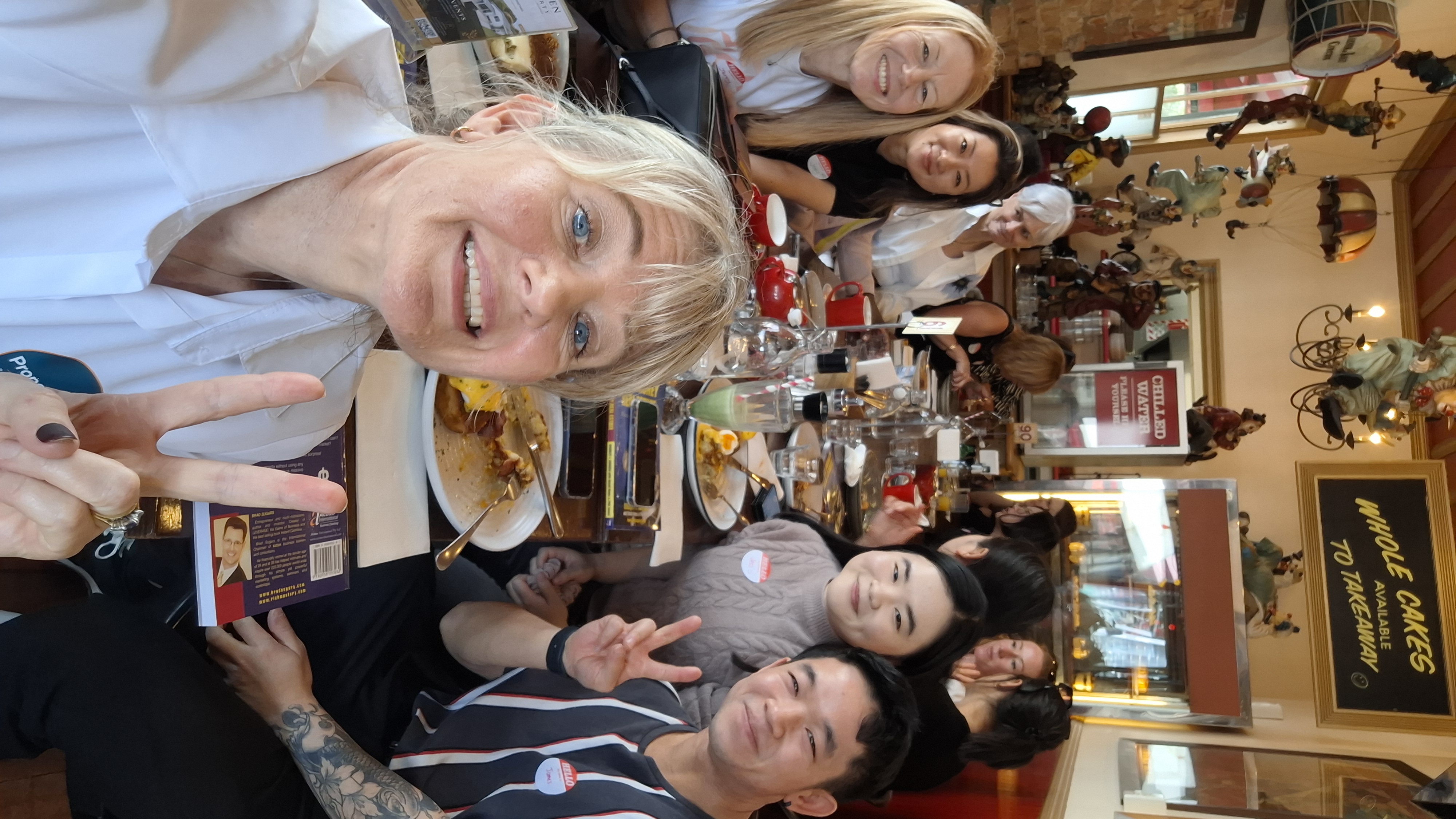 Host taking a peace-sign selfie with attendees along the full lunch table